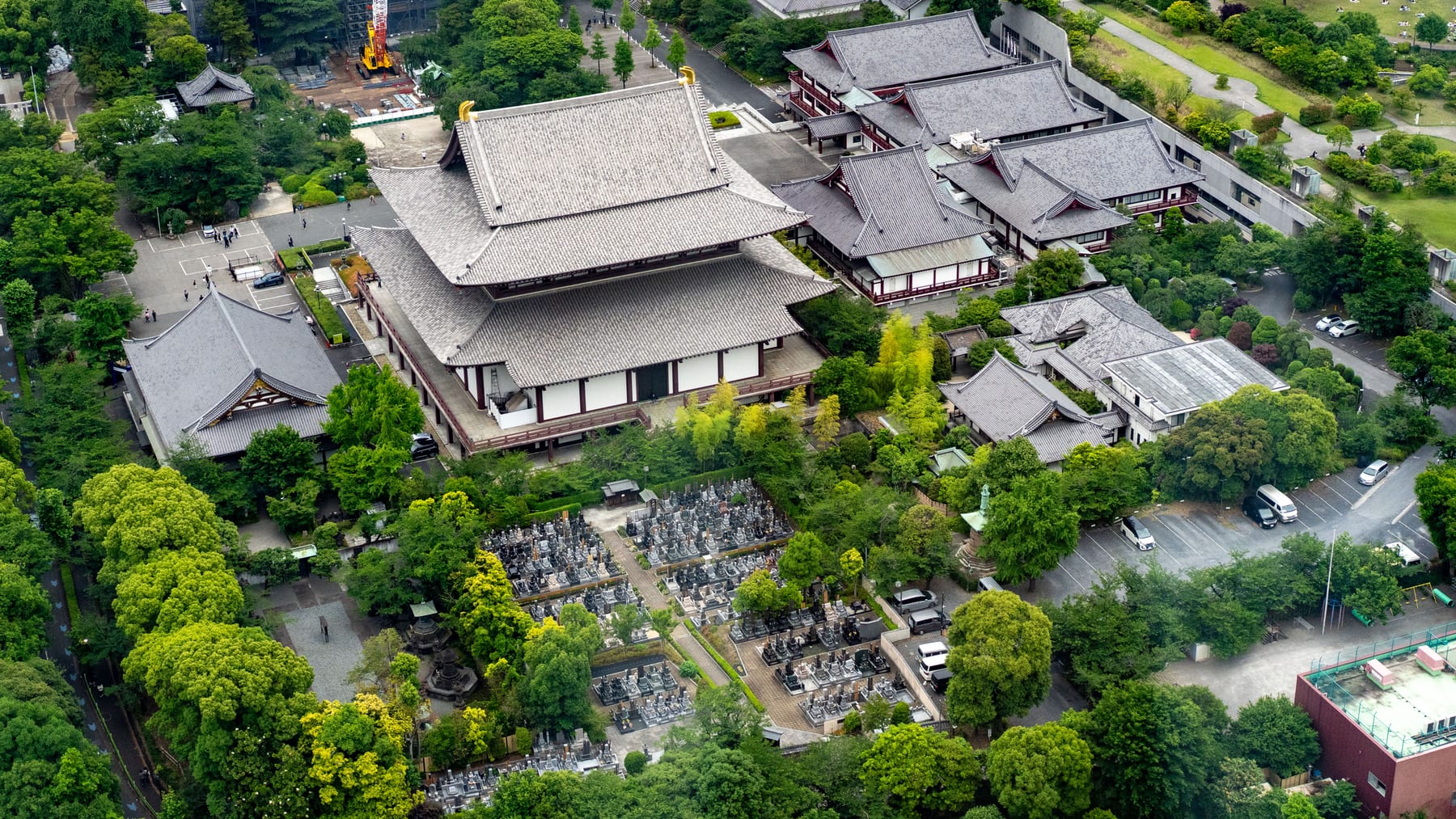 A graveyard surrounded by trees and temple roofs, seen from above amid a dense Tokyo cityscape.